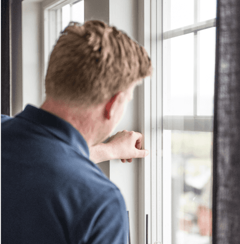 En ansatt i Takstcon undersøker vinduet i et hus.